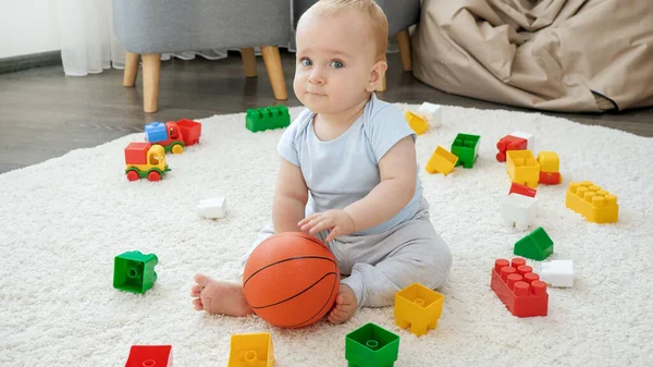 Uroczy 9-miesięczny chłopiec bawiący się piłką do kosza na dywanie w pokoju zabaw — Zdjęcie stockowe