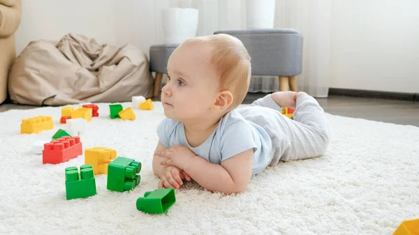 Cute chłopiec leżący na dywanie wśród kolorowych klocków i bloków zabawek — Zdjęcie stockowe