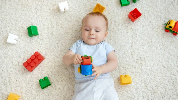 Ovanifrån av leende pojke liggande på matta i lekrum med massor av färgglada leksaker. Begreppet barns utveckling, utbildning och kreativitet i hemmet — Stockfoto