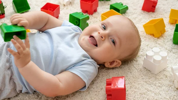 Uśmiechnięty chłopczyk i kupa zabawek na dywanie w pokoju zabaw. Koncepcja rozwoju, edukacji i kreatywności dzieci w domu — Zdjęcie stockowe