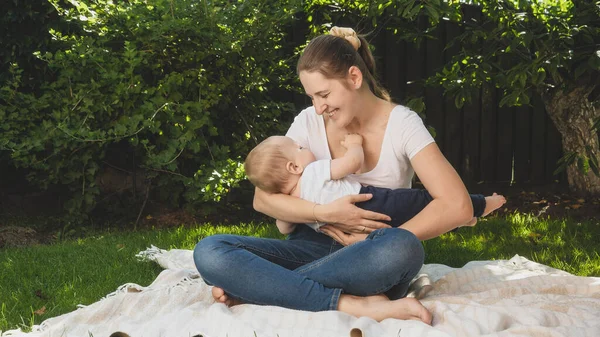 Feliz madre sonriente sosteniendo a su hijo bebé y sonriéndole en el jardín del patio trasero. Crianza, familia, desarrollo infantil y diversión al aire libre en la naturaleza. — Foto de Stock