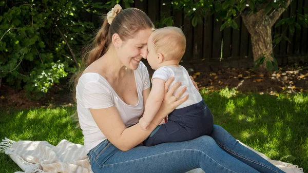 Sorrindo amorosa mulher abraçando e segurando seu filho bebê na grama no parque — Fotografia de Stock