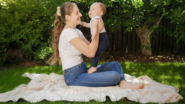 Lindo niño sonriente con la madre teniendo picnic en la manta en el jardín del patio trasero. Crianza, familia, desarrollo infantil y diversión al aire libre en la naturaleza. — Foto de Stock