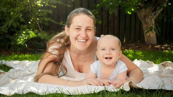 Portrét veselé usmívající se matky líbající svého chlapečka na trávě v zahradě. Rodičovství, rodina, vývoj dětí a zábava v přírodě. — Stock fotografie