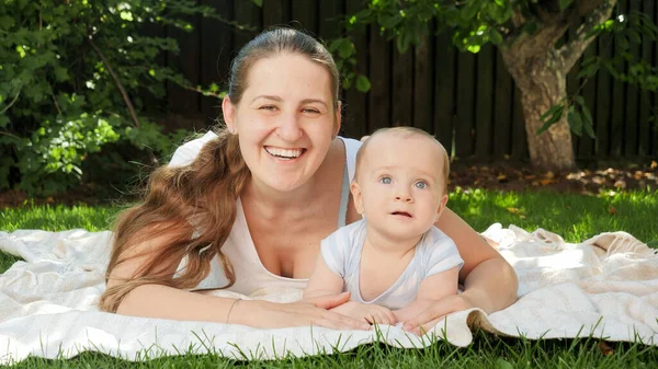 Portret van vrolijke jonge moeder liggend op gras in het park met haar kleine zoontje — Stockfoto