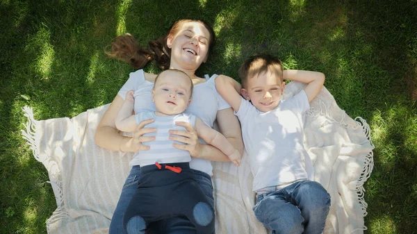 Enfants heureux avec mère relaxant sur l'herbe dans le parc et levant les yeux. Parentalité, famille, développement des enfants et plaisir en plein air dans la nature. — Photo