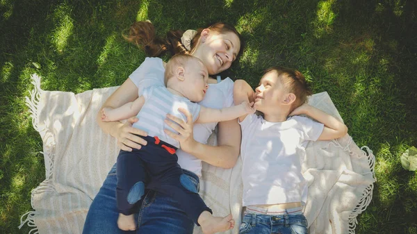 Toned retrato de crianças sorridentes deitado com a mãe na grama no parque — Fotografia de Stock