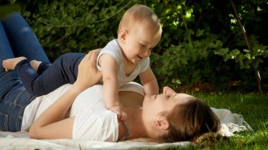 Parkta annesine uzanan mutlu, gülümseyen çocuk. Ebeveynlik, aile, çocuk gelişimi ve doğada eğlence..