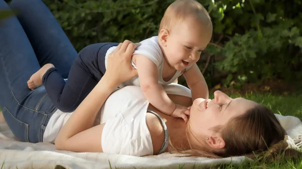 幸せな笑顔の女性は公園で草の上に横たわっていると彼女の小さな赤ちゃんの息子を保持 — ストック写真