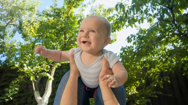 Punto de vista de la madre acostada en la hierba y levantando a su niño sonriente en el parque. Crianza, familia, desarrollo infantil y diversión al aire libre en la naturaleza. — Foto de Stock