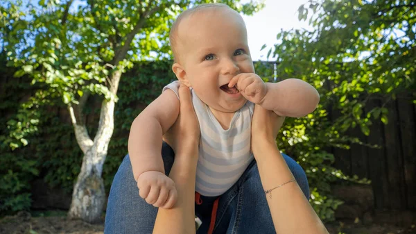 POV de pai segurando e levantando o bebê bonito filho no jardim. Paternidade, família, desenvolvimento infantil e diversão ao ar livre na natureza. — Fotografia de Stock