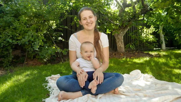 Retrato de mamá sonriente y alegre con el niño sentado en la hierba y sonriendo en la cámara. Crianza, familia, desarrollo infantil y diversión al aire libre en la naturaleza. — Foto de Stock