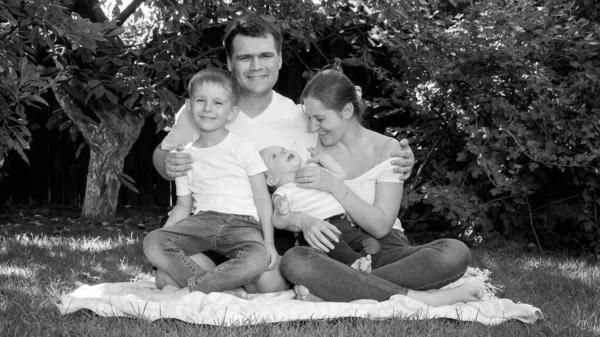 Retrato en blanco y negro de una familia feliz y cariñosa relajándose en la hierba en el parque en las vacaciones de verano — Foto de Stock