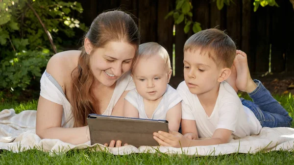 Mère souriante joyeuse avec deux fils allongés sur de l'herbe et utilisant une tablette numérique. Parentalité, famille, développement des enfants et technologie — Photo