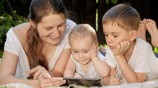 Retrato divertido de lindo bebé con la familia acostada en la hierba y el uso de la tableta en el parque — Foto de Stock