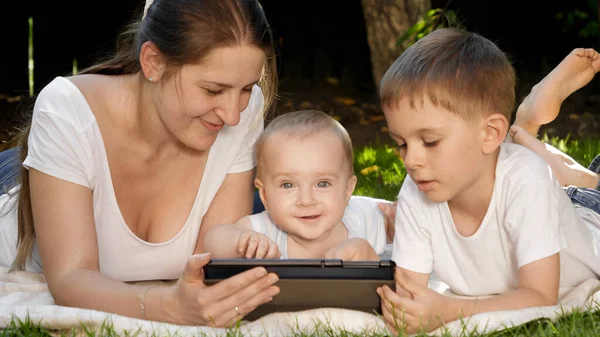 Lindo niño pequeño con la familia acostada en la hierba en el parque con la computadora de la tableta. Crianza, desarrollo familiar, infantil y tecnología — Foto de Stock