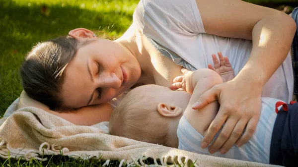 Retrato de lindo bebé niño acostado con la madre en la hierba y chupando la leche materna —  Fotos de Stock