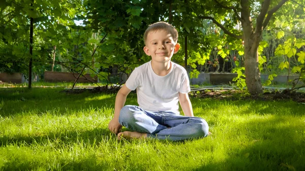 Ritratto di ragazzo sorridente seduto sull'erba nel giardino del cortile della casa nella soleggiata giornata estiva — Foto Stock