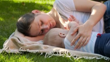 Güzel, genç bir anne çimenlerde uzanıyor ve bebeğini anne sütüyle besliyor. Ebeveynlik, aile, çocuk gelişimi ve doğal beslenme.