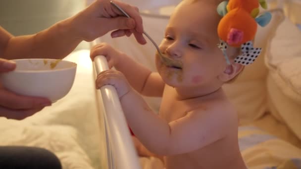 Portrait de bébé garçon sale et salissant mangeant de la soupe de cuillère au lit la nuit. Concept de nutrition saine, de responsabilités parentales et de soins aux bébés — Video