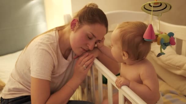 Fáradt anya elaludt a kisfia bölcsője mellett éjszaka. A szülői, szülői fáradtság és a gyermekek fejlődésének fogalma. — Stock videók