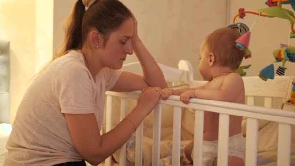 Moe slaperige moeder schommelende wieg van haar baby huilen en weigeren om te slapen 's nachts. Begrip ouderschap, oudervermoeidheid en ontwikkeling van kinderen. — Stockvideo