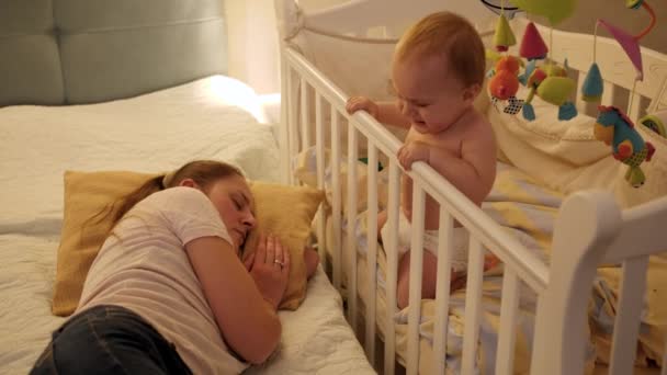 Ung trött mamma somnade bredvid sitt barn gråtande i sängen. Begreppet föräldraskap, föräldratrötthet och barns utveckling. — Stockvideo