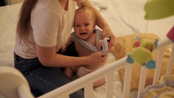 Jeune mère changeant de clithes et habillant son bébé fils dans son lit la nuit. Concept de parentalité, fatigue des parents et développement des enfants. — Video