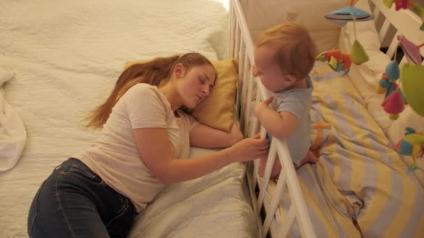Müde müde Mutter schaukelt Babybett und schläft. Konzept der Elternschaft, der Müdigkeit der Eltern und der Entwicklung der Kinder. — Stockvideo