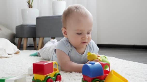 Pequeño niño jugando con coloridos coches de juguete en la alfombra en la sala de estar. Concepto de desarrollo infantil, educación y creatividad en el hogar — Vídeo de stock