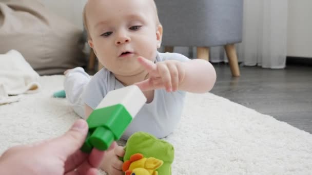 Närbild av förälder som ger plast leksaksblock till liten pojke spelar på mattan. Begreppet barns utveckling, utbildning och kreativitet i hemmet — Stockvideo