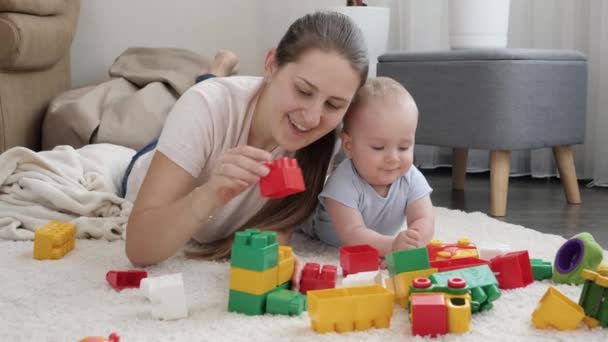 Glücklich lächelnde Mutter mit Baby-Sohn baut Spielzeugturm aus bunten Ziegeln und Bauklötzen. Konzept der Entwicklung, Bildung und Kreativität von Kindern zu Hause — Stockvideo
