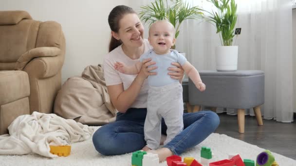 Bonito menino sorridente em pé na sala de estar e olhando para brinquedos coloridos. Conceito de desenvolvimento infantil, educação e criatividade em casa — Vídeo de Stock