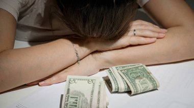 Büyük borcu ve maddi sorunları olan stresli bir kadın birkaç para banknotunun yanında yatıyor.