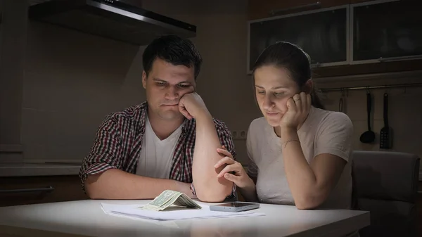 Casal perturbado calculando o orçamento familiar e olhando para poucas notas de dinheiro na tabela — Fotografia de Stock