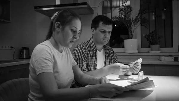 Schwarz-Weiß-Porträt eines besorgten und gestressten Paares, das nachts in der Küche Geld zählt — Stockfoto