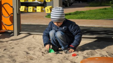 Küçük çocuk oyun parkında kum havuzunda oynuyor. Çocuk gelişimi, spor ve eğitim kavramı.