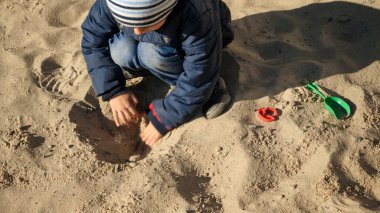 Küçük çocuk kürekle kum kazıyor ve parkta oyun oynuyor. Çocuk gelişimi, spor ve eğitim kavramı.