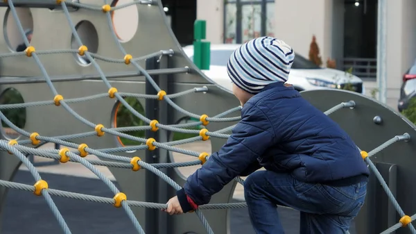 Gelukkige lachende jongen spelen op de speelplaats en klimmen op touw net. Concept van kinderontwikkeling, sport en onderwijs. — Stockfoto