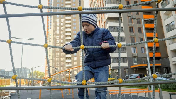 Szczęśliwy uśmiechnięty chłopiec wspinający się po sieci na dziecięcy plac zabaw. Koncepcja rozwoju dzieci, sportu i edukacji. — Zdjęcie stockowe