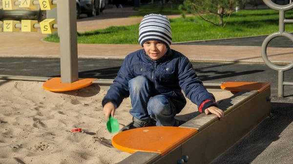 Liten pojke leker i sandlåda med leksak plast spade i parken — Stockfoto