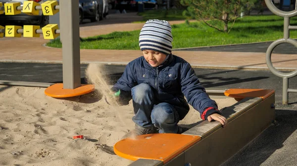 Mały chłopiec bawiący się w piaskownicy na placu zabaw w parku i kopiący piasek łopatą zabawki — Zdjęcie stockowe