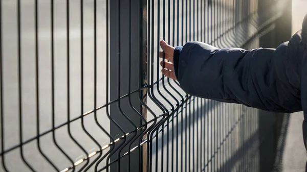 Closeup of little boy walking by the metal fence and touching it with hand. Concept of poverty, immigration, bullying and kids stress — Stock Photo, Image
