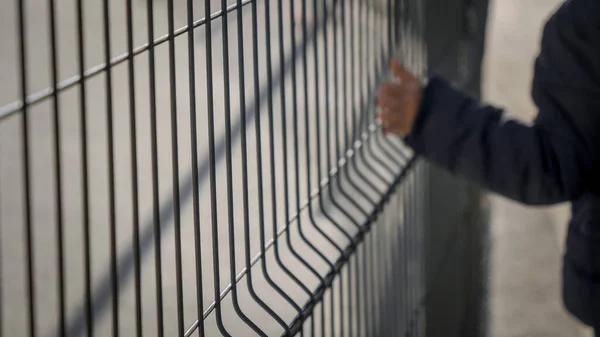 BLurred ur fokus iamge av pojke promenader av ht emetal staket och vidröra nät med handen — Stockfoto