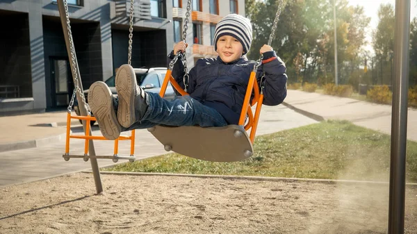 Glimlachend jongetje zwaaiend op de schommel in de speeltuin. Concept van kinderontwikkeling, sport en onderwijs. — Stockfoto
