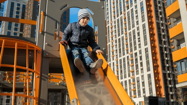 Happy smiling boy riding down slide on modern children playground — Stock Photo, Image