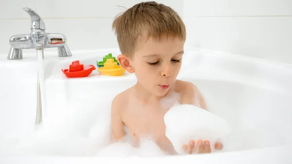 Feliz chico sonriente bañándose y jugando con espuma de jabón. Concepto de hygine, desarrollo infantil y diversión en casa — Foto de Stock