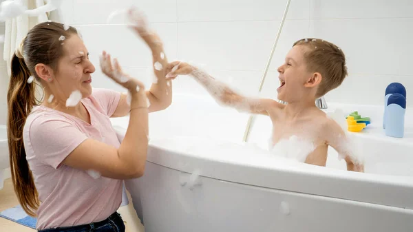 Glücklich lachende und lächelnde Mutter mit Sohn, die im Bad mit Seifenschaum spielt. Konzept aus Hygiene, kindlicher Entwicklung und Spaß zu Hause — Stockfoto