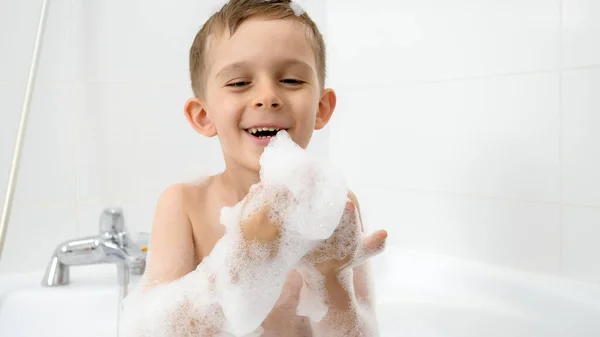 Menino bonito soprando sabão suda das mãos enquanto se lava no banho. Conceito de hygine, desenvolvimento infantil e diversão em casa — Fotografia de Stock