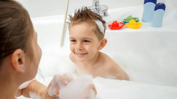 Lindo niño sonriente lavándose en el baño y mirando a su joven madre — Foto de Stock